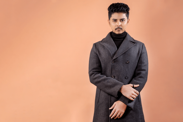 Sophisticated portrait of a man wearing a gray overcoat against a warm backdrop.
